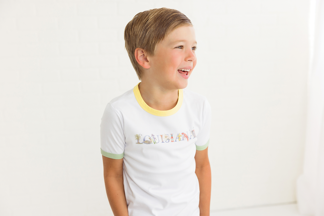 White kids tee with yellow collar, green sleeve cuffs, and Louisiana front graphic
