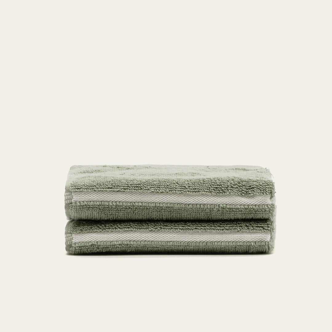 Sage green cotton towel set, neatly folded stack of four with stitched edges.
