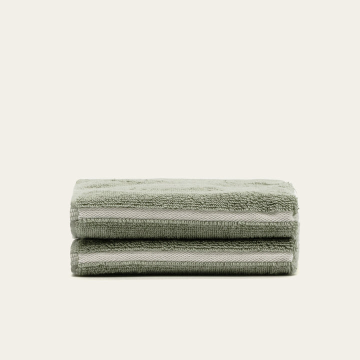 Sage green cotton towel set, neatly folded stack of four with stitched edges.