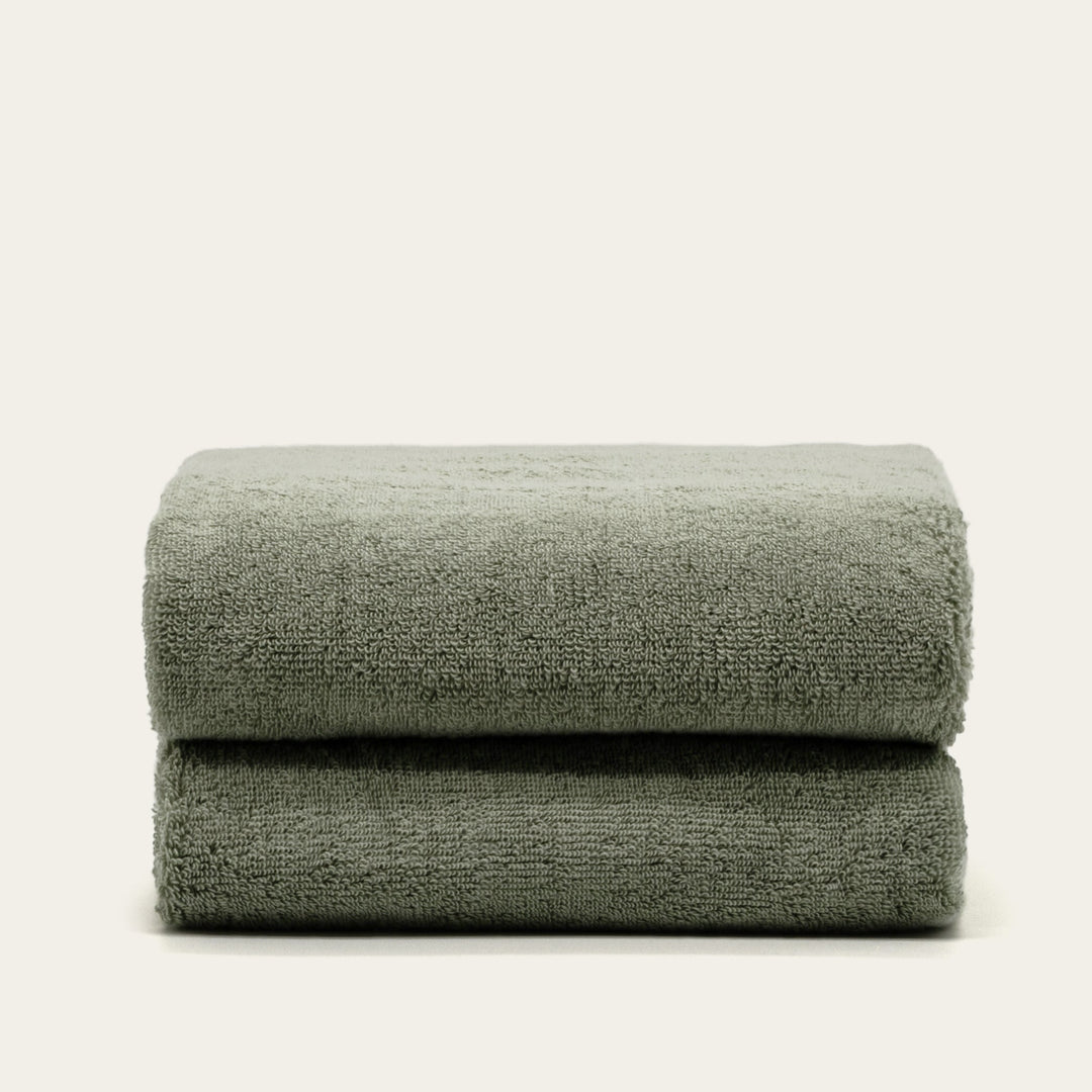 Sage green cotton towels, pair of folded terry towels with plush texture.