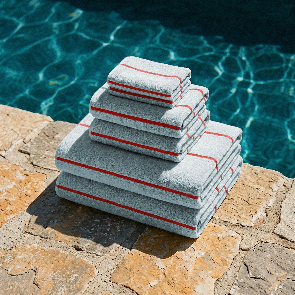 Stack of gray cotton towels with red striped borders, folded on a stone poolside.