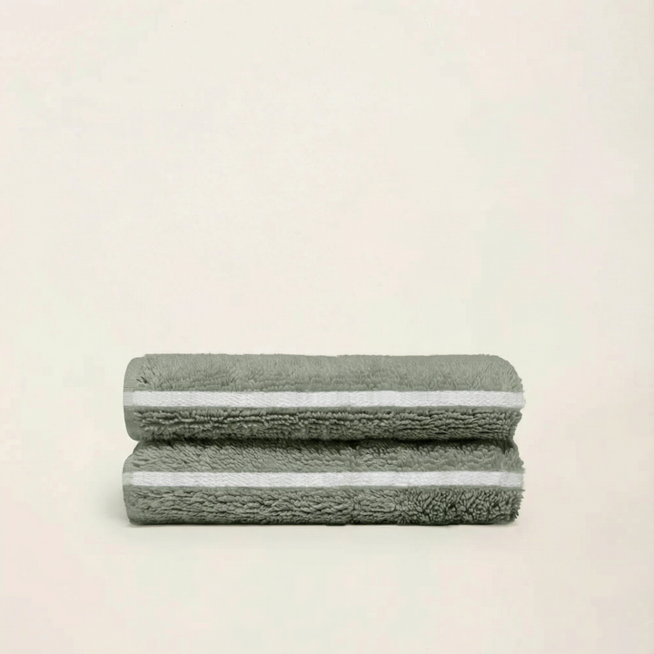 Two folded sage green cotton towels with subtle ecru-edged trim