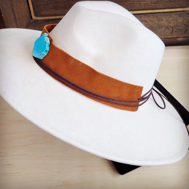 Tan suede hat band with turquoise patch and tied cords on white felt hat