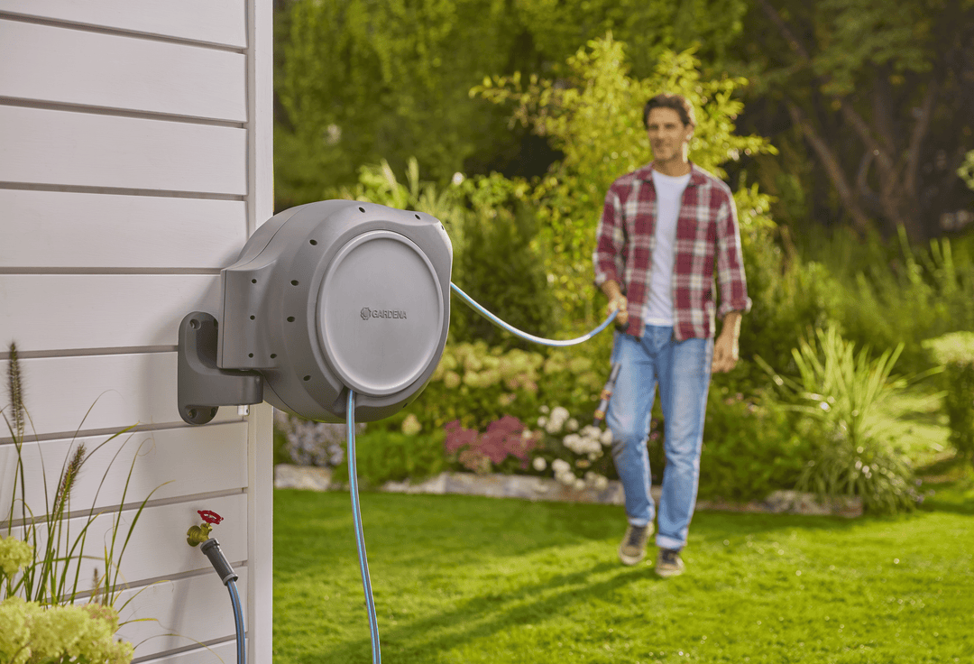 Wall-mounted retractable hose reel with blue hose extended toward yard watering