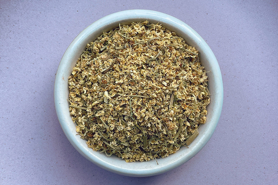 Dried elderflower buds in a white ceramic bowl, ready for herbal tea