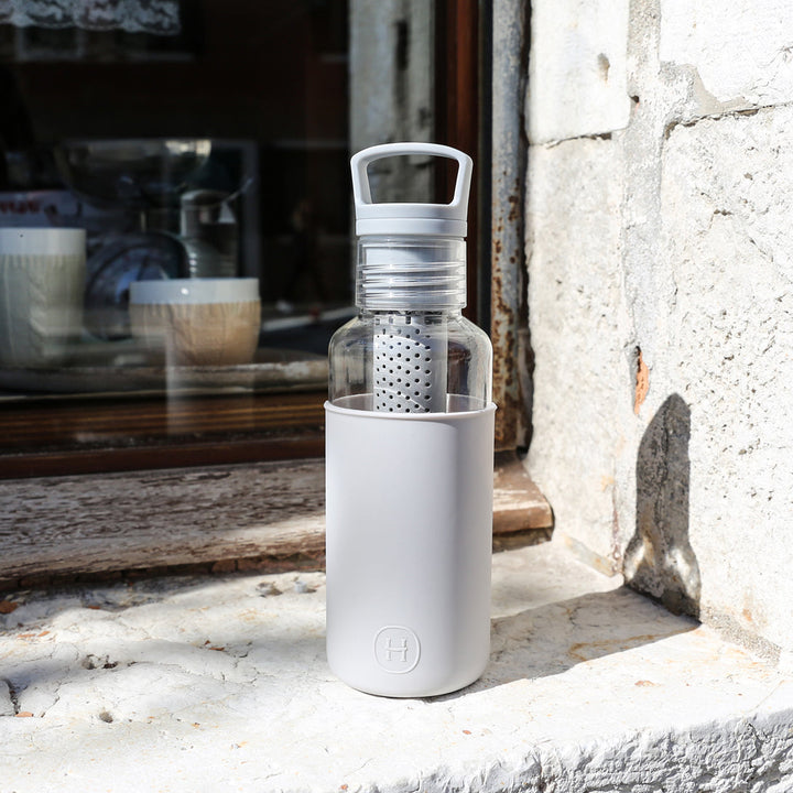 20 oz grey insulated bottle with flip-top lid and clear infuser on stone ledge