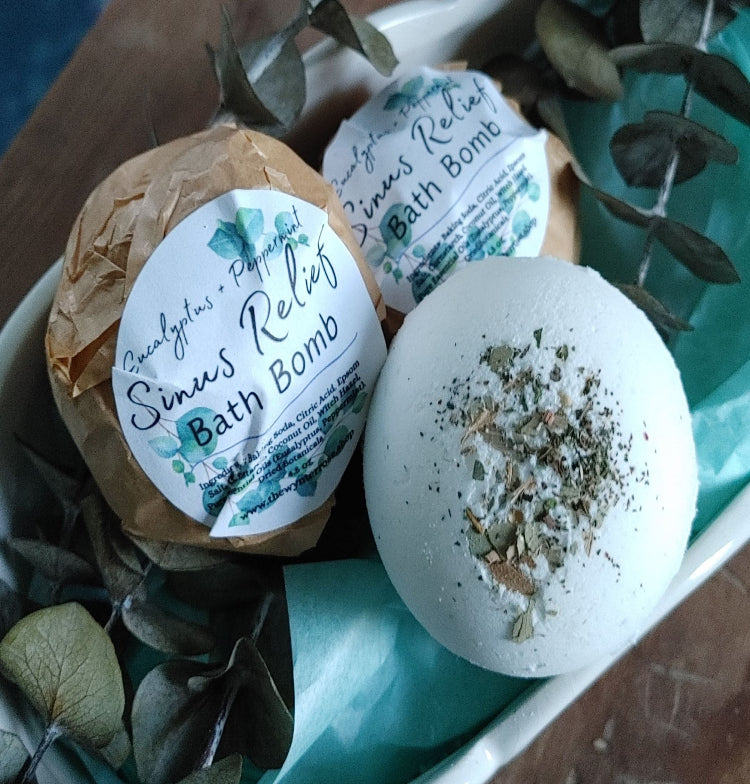 Two white bath bombs with eucalyptus peppermint labels and herb speckles in tray