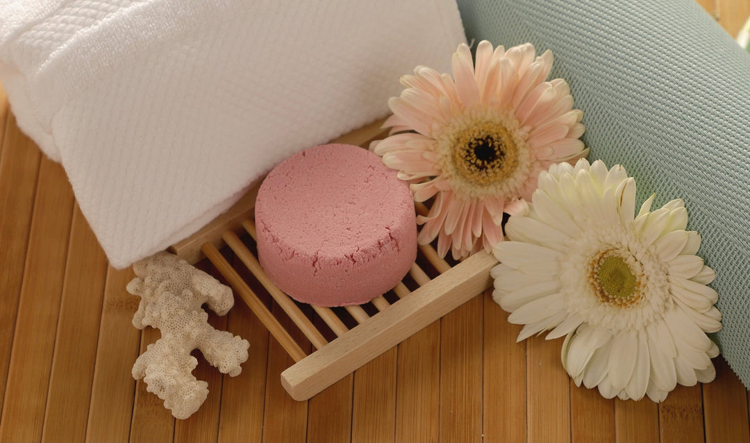 Pink round shampoo bar on a wooden tray with white and peach flowers