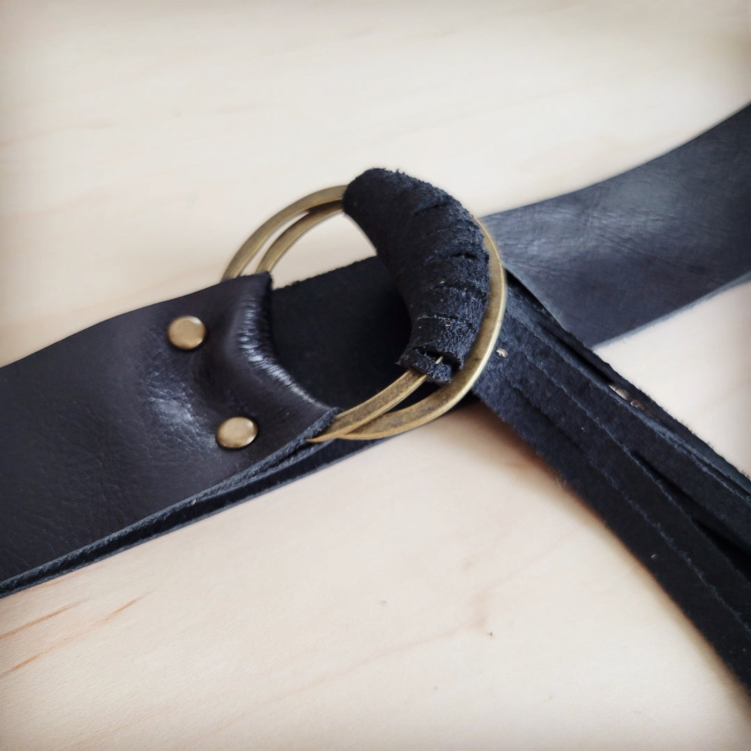 Black leather belt close-up with round ring buckle, padded loop, and fringe strips