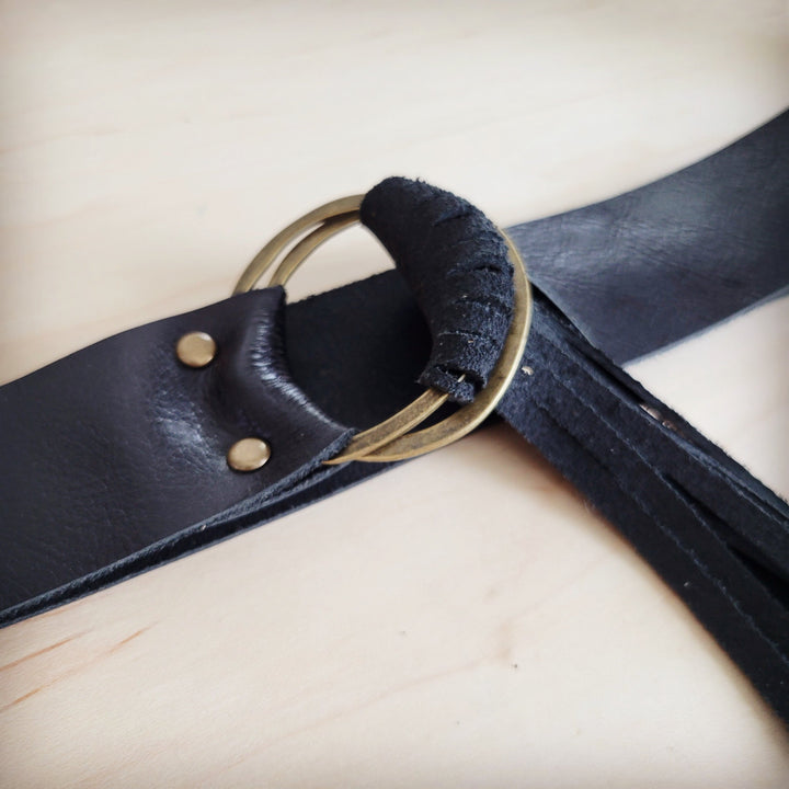 Black leather belt close-up with round ring buckle, padded loop, and fringe strips
