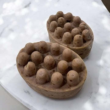 Dark massage bar soap with rounded nodules in a small bowl