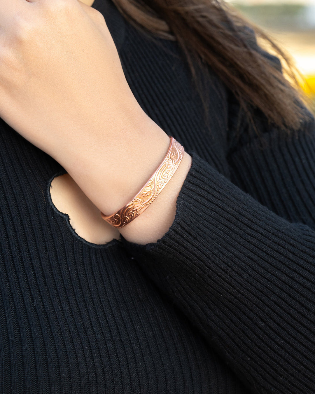 Rose copper floral cuff bracelet on wrist, close-up of engraved leaf texture