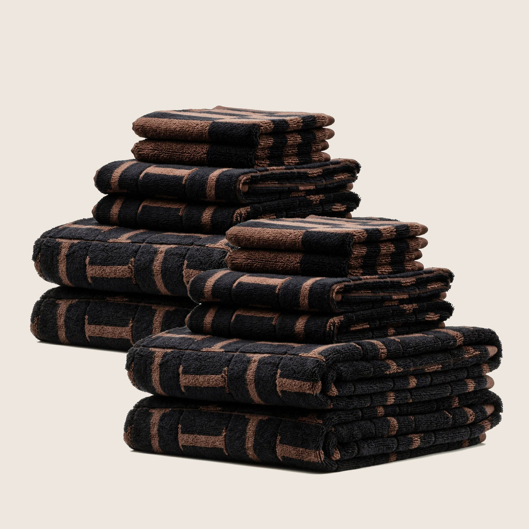 Multiple folded cotton towels stacked, dark with brown check-style stripe pattern
