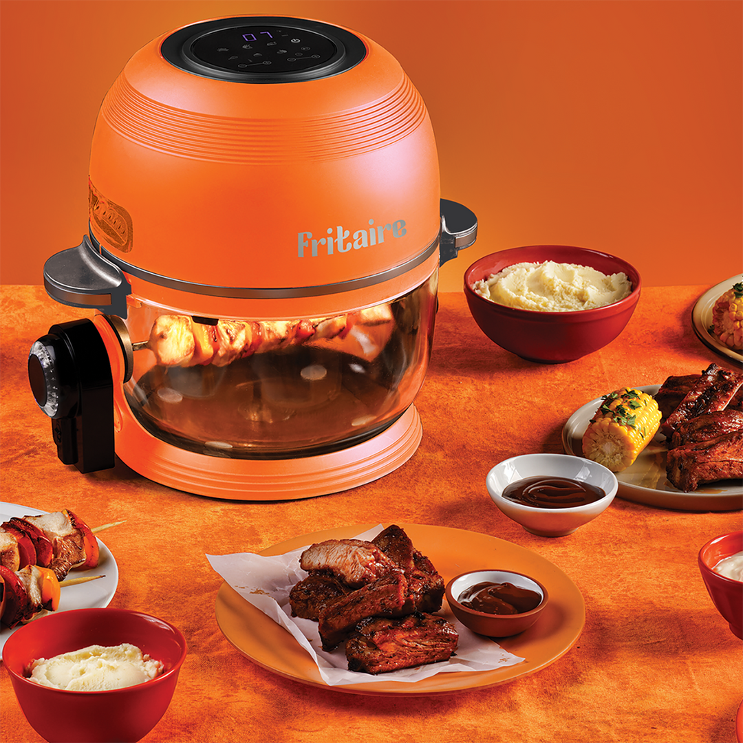 Orange air fryer with clear glass bowl and plates of cooked chicken and fries