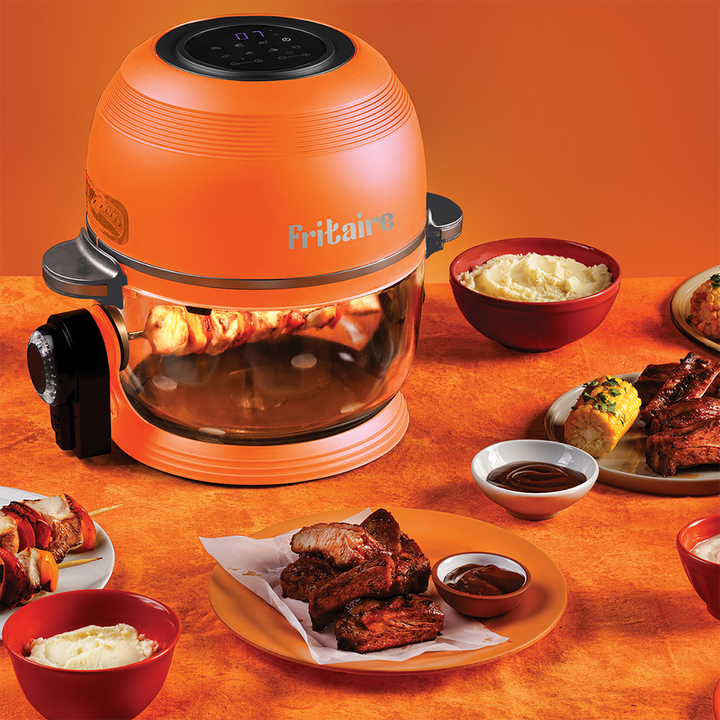 Orange air fryer with clear glass bowl and plates of cooked chicken and fries