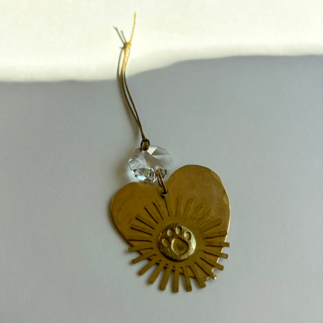 Heart-shaped gold ornament with sunburst detail, hanging crystal and ribbon loop