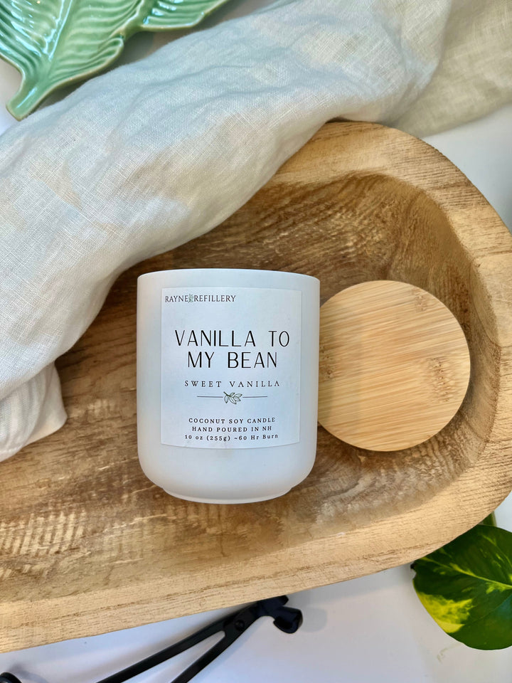 Vanilla coconut soy candle in white jar with wooden lid on round wooden tray