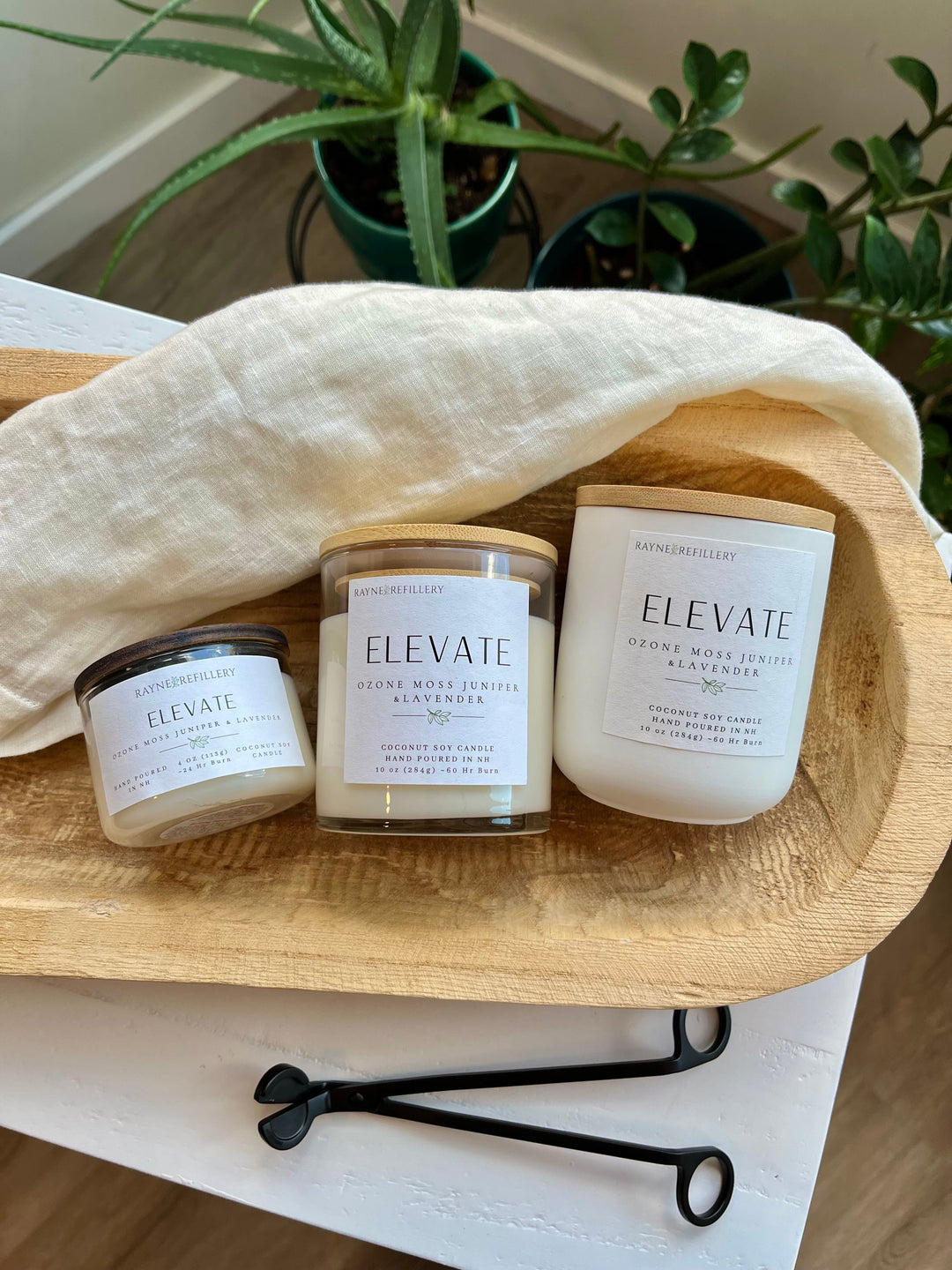 Three coconut soy candles in glass jars with black wick trimmer on a wooden tray