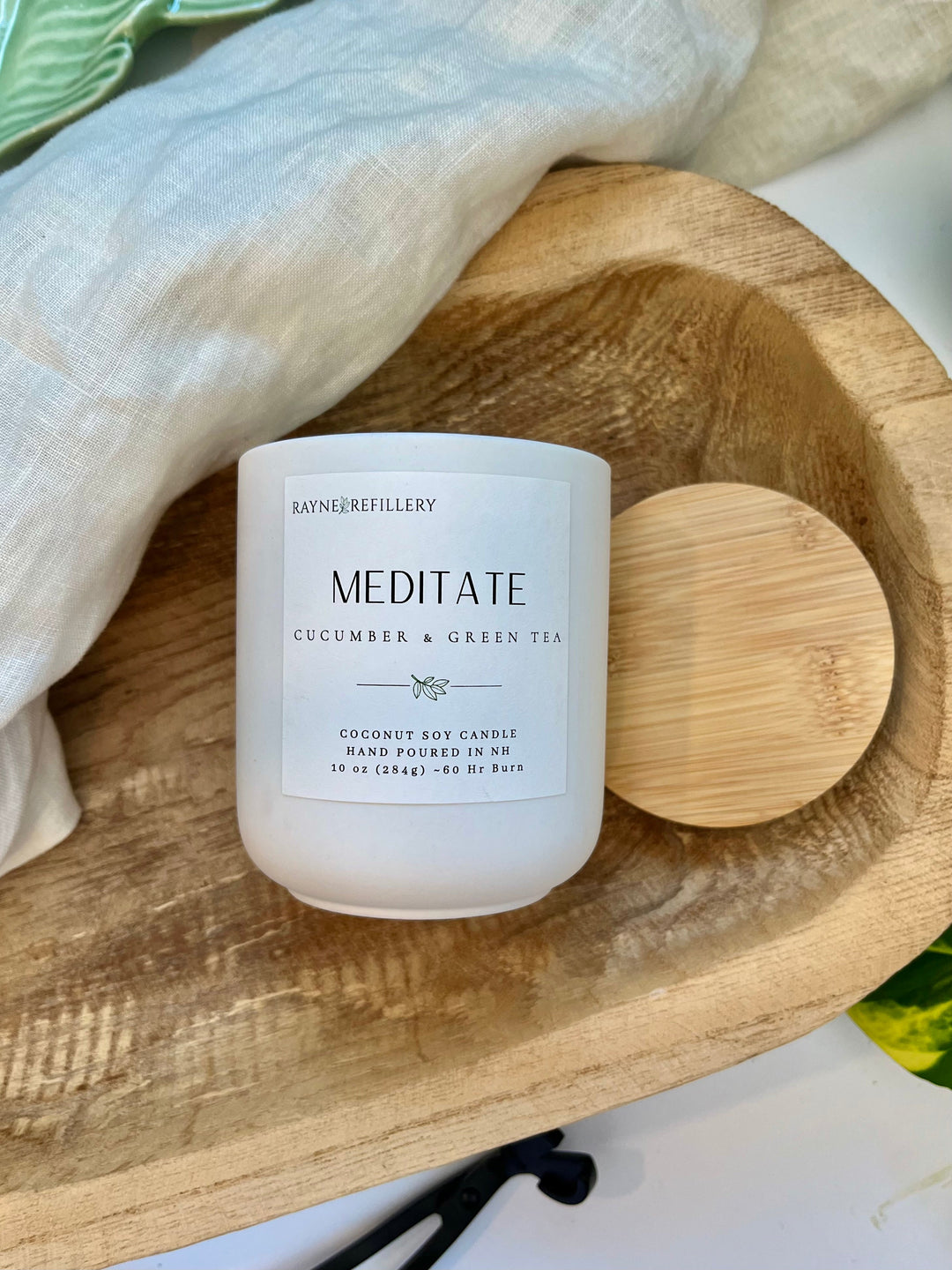 Coconut soy candle in white glass jar with bold black text label, wood lid behind