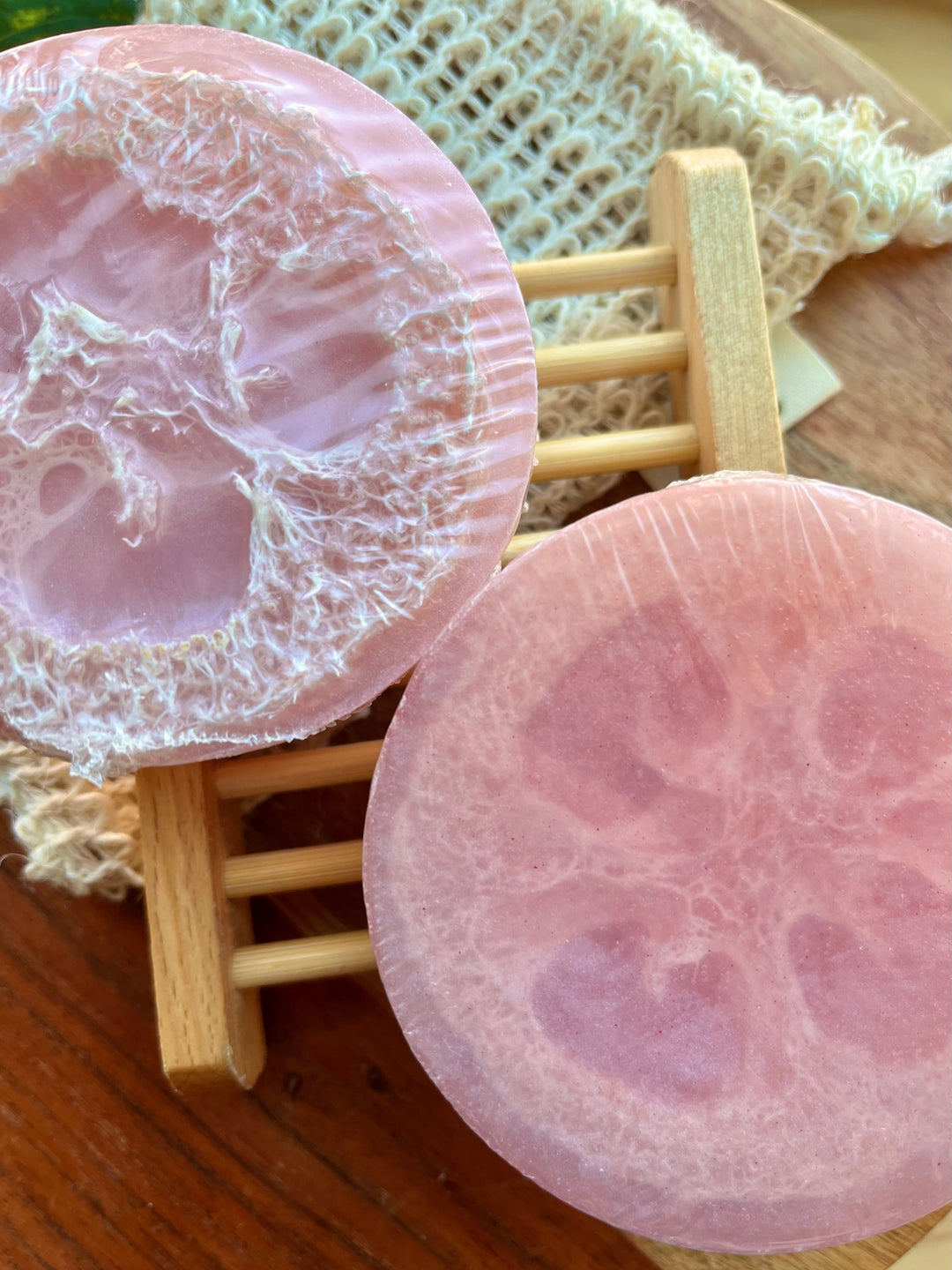 Round pink soap bar on wooden slats, close-up with foamy exfoliating texture