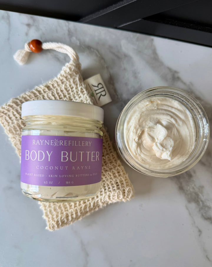 Coconut body butter jar with white lid and a scoop of creamy balm in a glass container