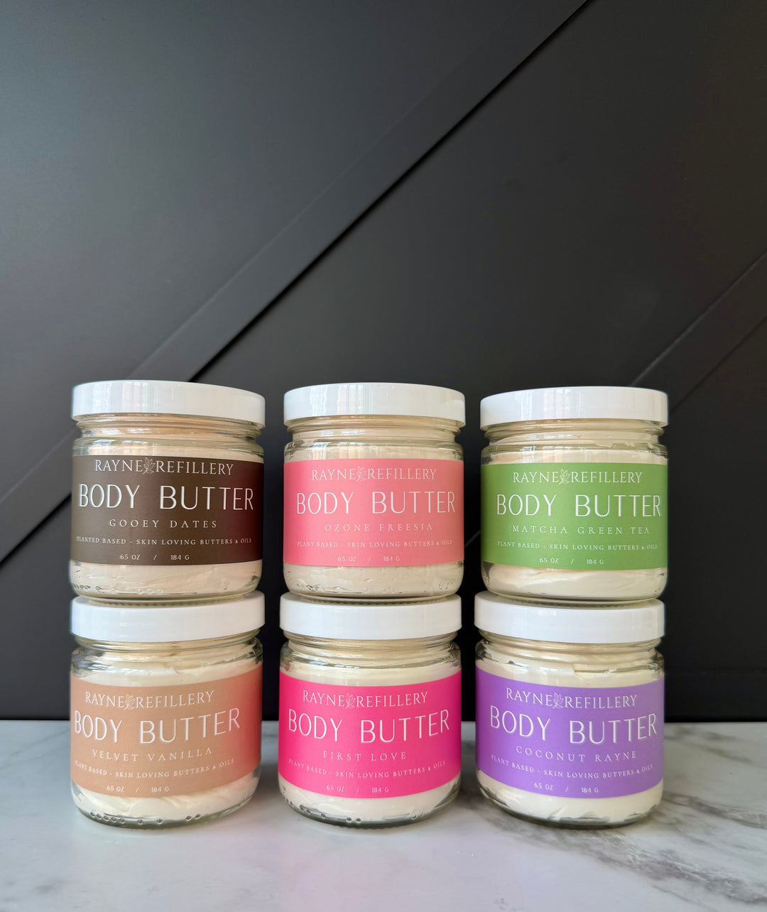 Set of body butter jars in beige, pink, and green tones on a countertop