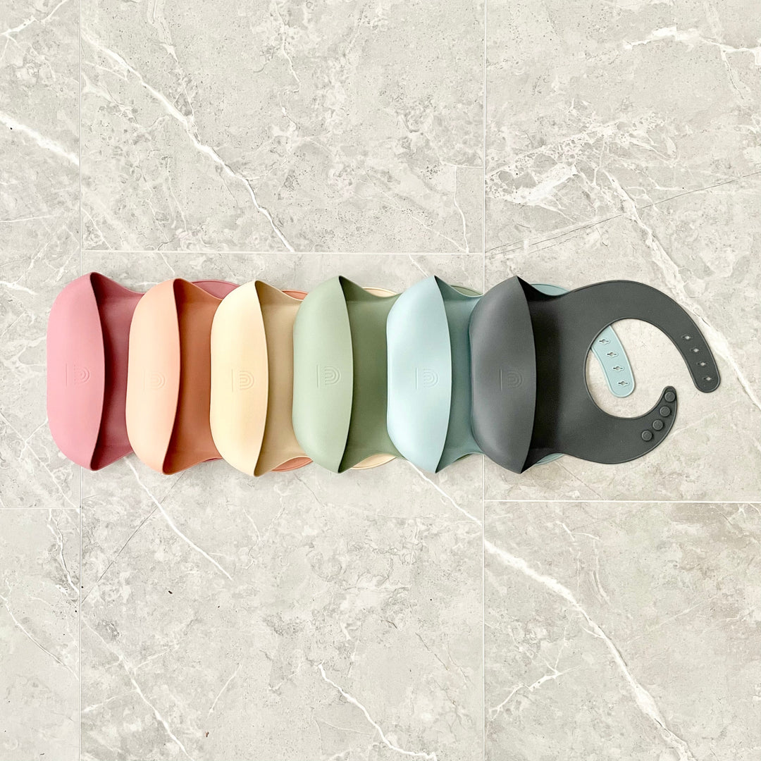 Set of silicone bucket bibs in multiple colors lined up, with snap buttons