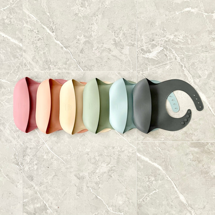 Set of silicone bucket bibs in multiple colors lined up, with snap buttons