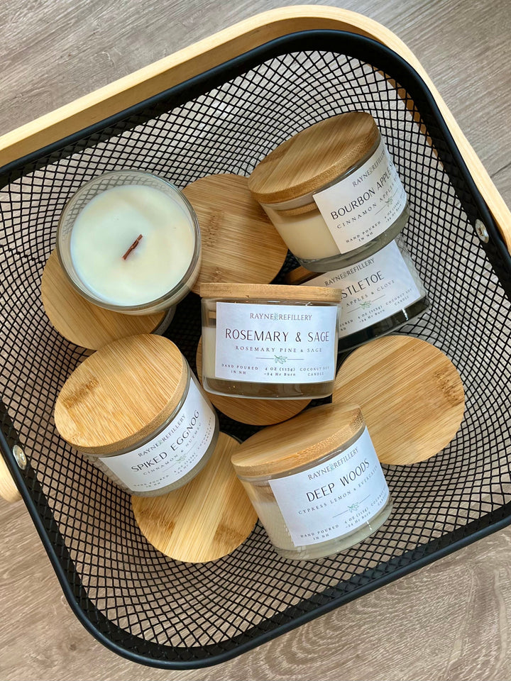 Assorted coconut soy candles in white glass jars with wood lids on black mesh tray