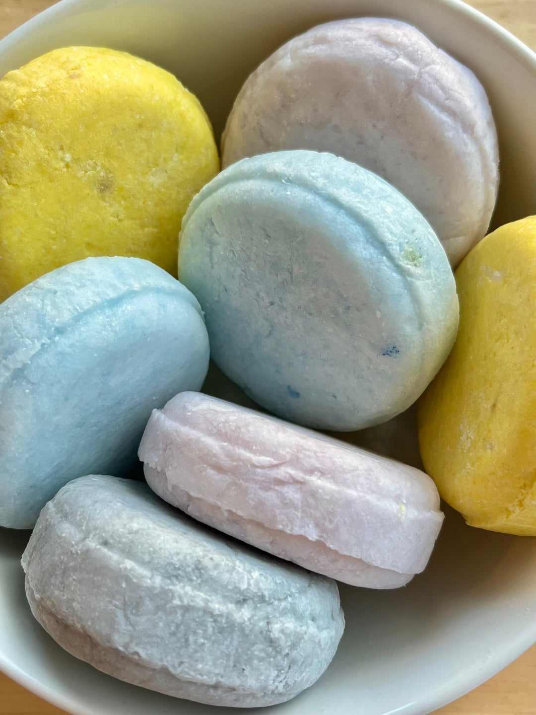 Assorted solid shampoo bar pieces in a bowl, pastel blue, yellow, gray and pink