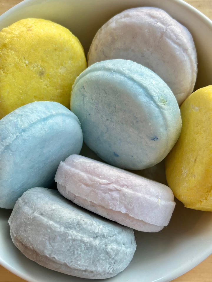 Assorted solid shampoo bar pieces in a bowl, pastel blue, yellow, gray and pink