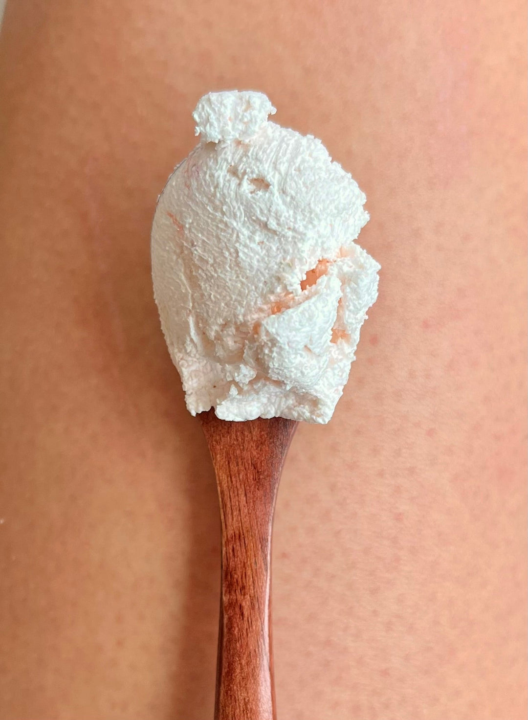 Whipped exfoliating scrub on a wooden applicator, pale pink and grainy