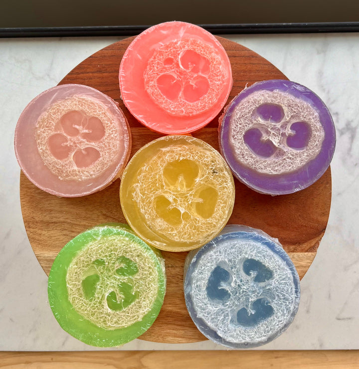 Loofah soap bar assortment on wooden tray, including pink, purple, yellow, green and blue