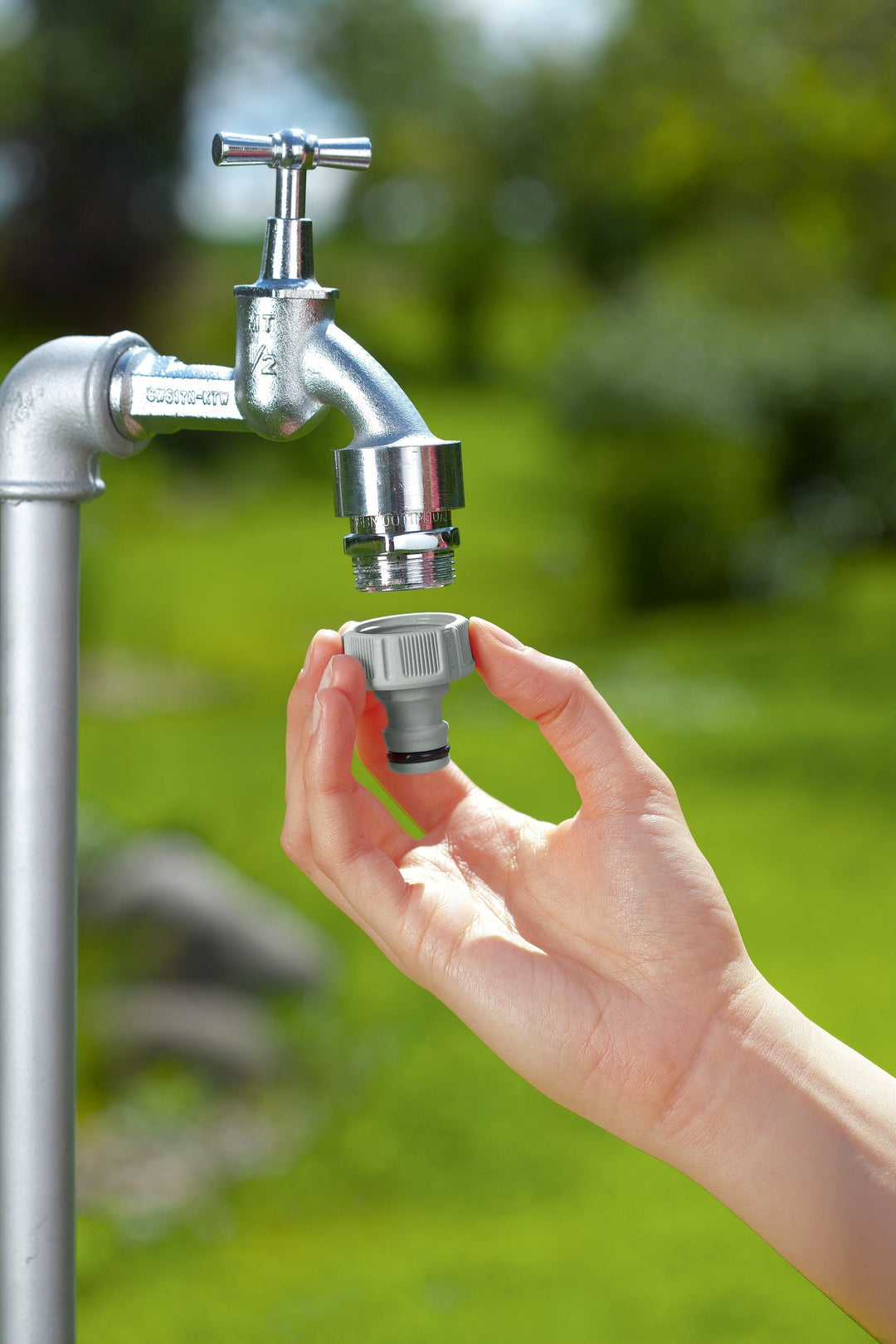 Faucet quick adapter being installed on outdoor tap with visible hands and connection