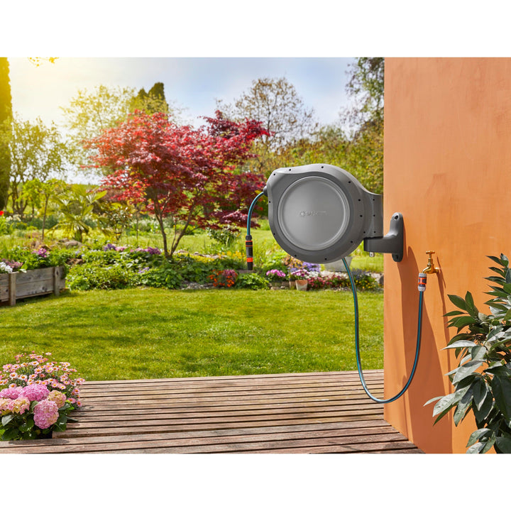 Retractable hose reel with gray housing and blue hose spraying outdoors from wall mount