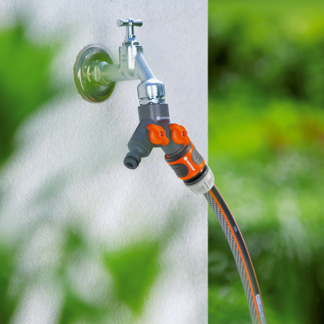 Twin-tap hose connector with two orange valves on two hoses from a wall spigot