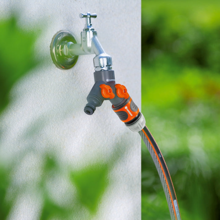 Twin-tap hose connector with two orange valves on two hoses from a wall spigot