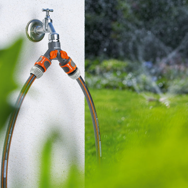 Twin-tap garden hose connector with orange valves, connected to a wall water tap