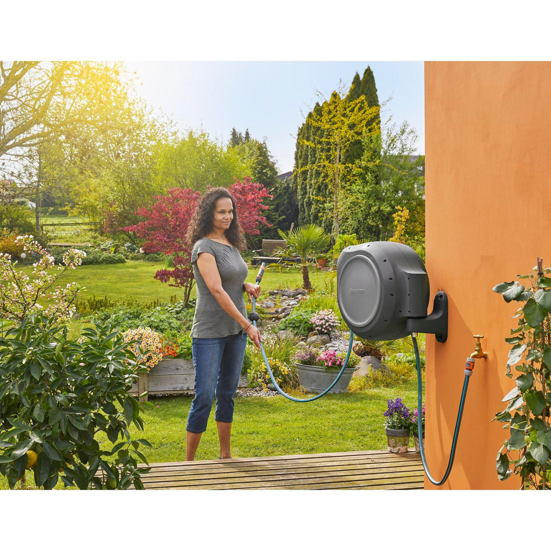 Wall-mounted gray hose reel on orange exterior wall with blue hose and sprayer