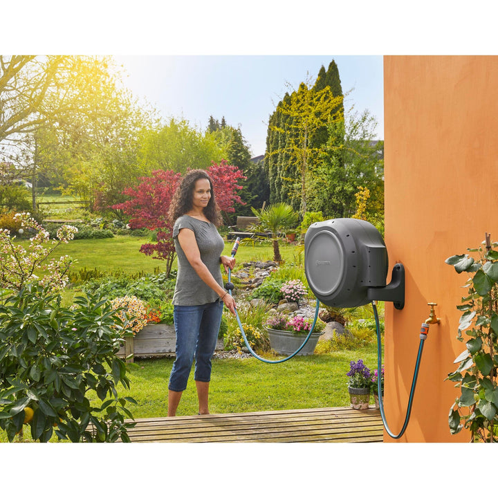 Wall-mounted gray hose reel on orange exterior wall with blue hose and sprayer