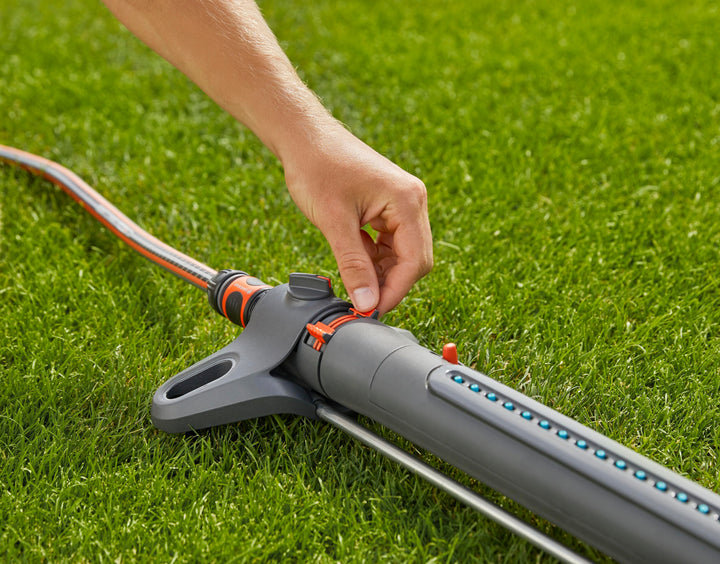 Hand adjusting oscillating sprinkler on green lawn, with orange dial