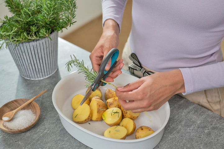 Herb scissors with teal-and-black ergonomic handles cutting ingredients in a bowl