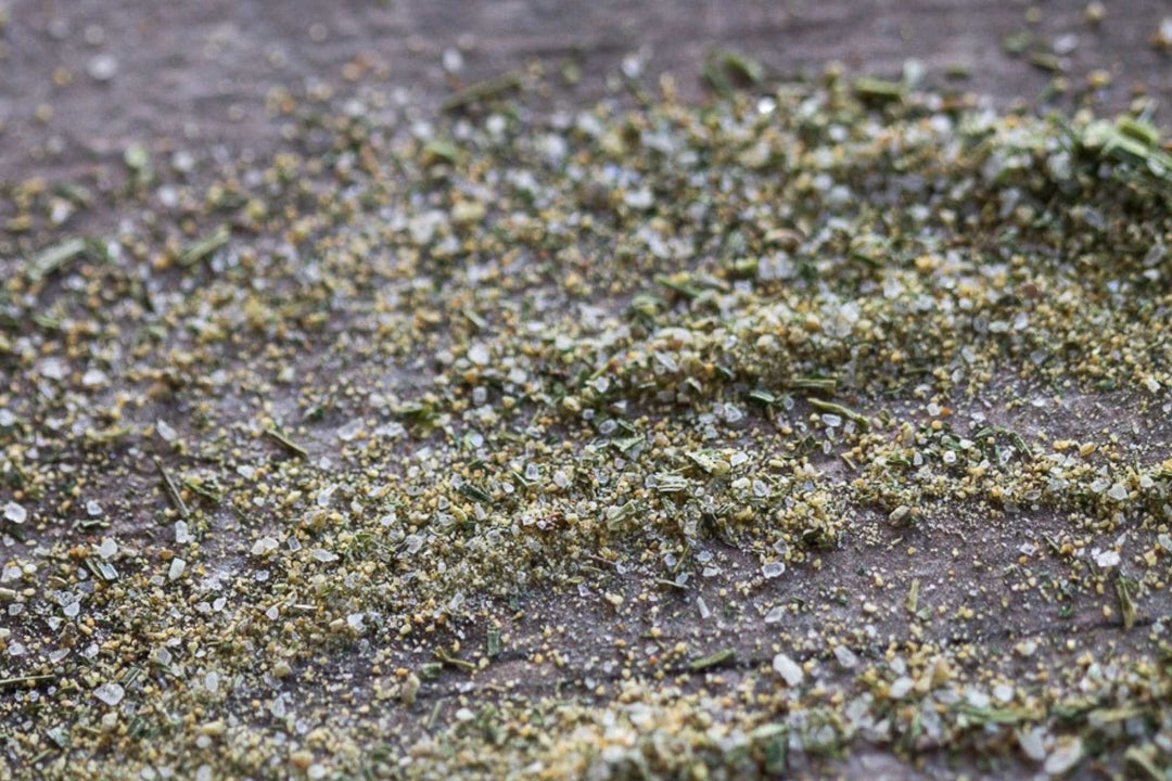 Dried herb seasoning flakes in green and gray on a dark textured surface