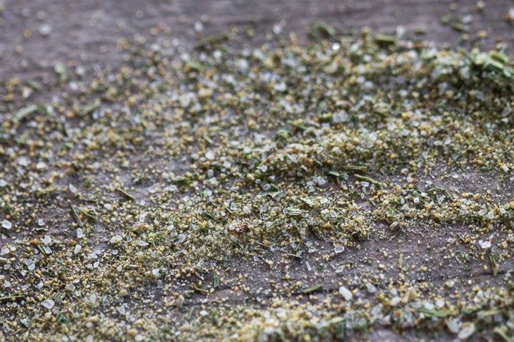Dried herb seasoning flakes in green and gray on a dark textured surface
