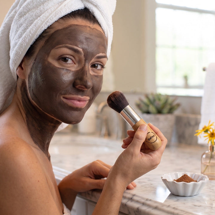 Spa facial mud mask on face, applying with makeup brush while wearing a head towel