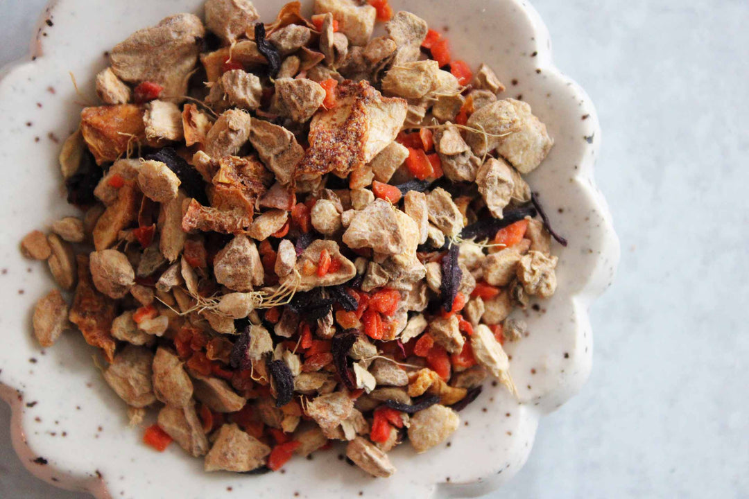 Dried ginger and spice tea blend in a shallow bowl, with small vegetable bits
