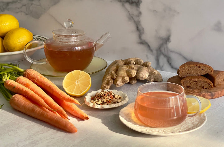 Glass teacups and teapot with ginger and carrot, plus lemon slices on tray