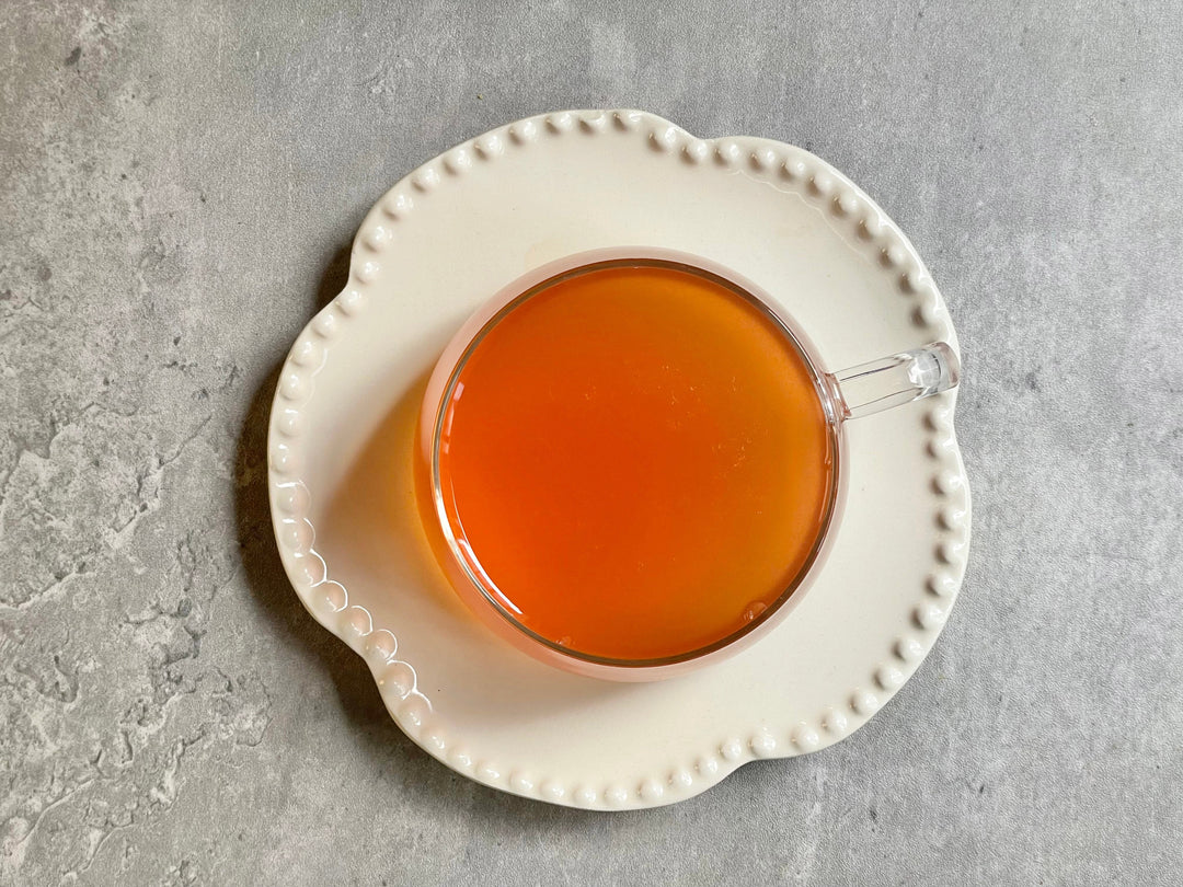 Glass cup of amber-orange ginger tea on a white plate
