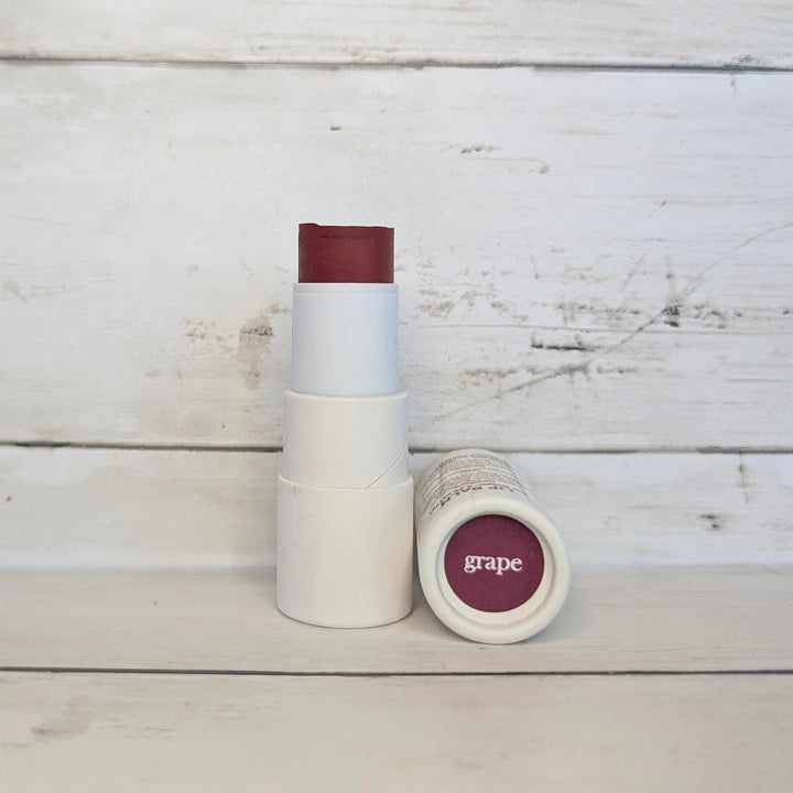 2-in-1 lip and cheek tint lipstick in Grape, white tube with maroon cap and open purple pan