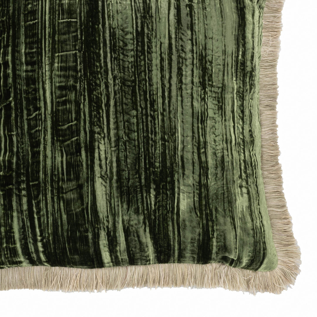 Green velvet pillow corner detail with beige fringe trim and vertical ribbed texture.